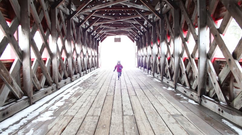 Toddler running inside a covered bridge.